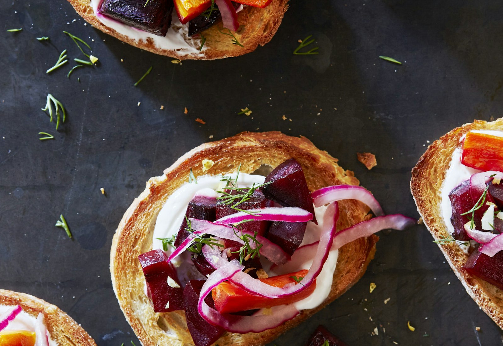 Borscht crostinis garnished with dill atop black surface.