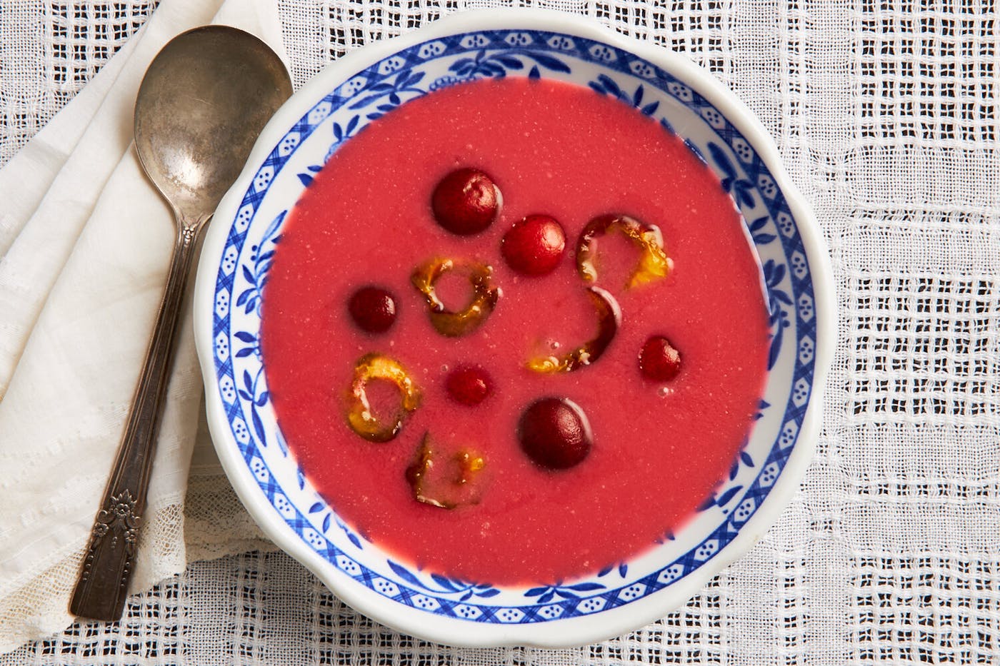 Cherry soup with halved cherries in blue patterned bowl atop woven white tablecloth.