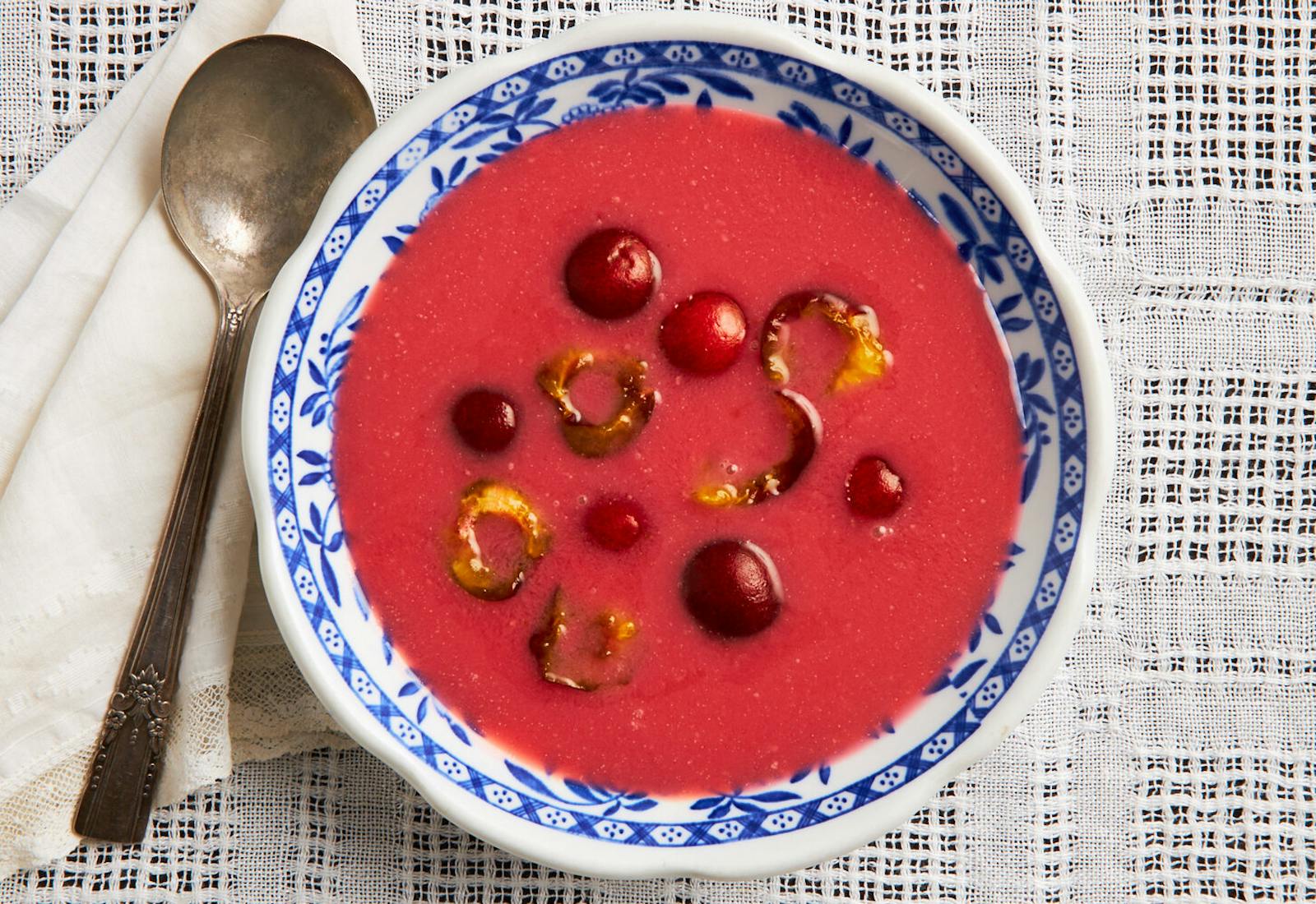 Cherry soup with halved cherries in blue patterned bowl atop woven white tablecloth.
