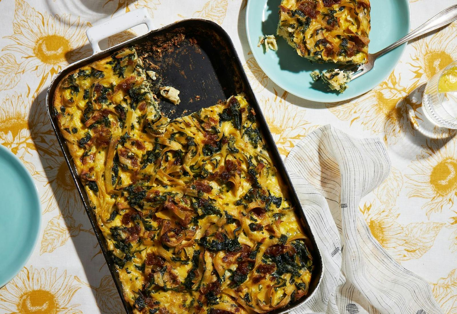 Onion and spinach kugel in white casserole pan atop floral tablecloth.