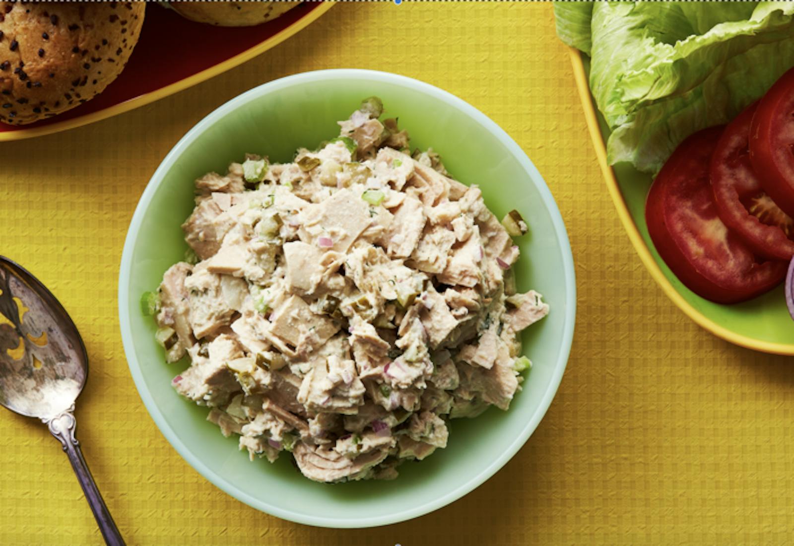 Tuna fish salad in green bowl with seeded bagels, lettuce, tomato and onion.