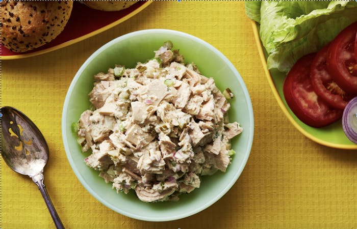 Tuna fish salad in green bowl with seeded bagels, lettuce, tomato and onion.