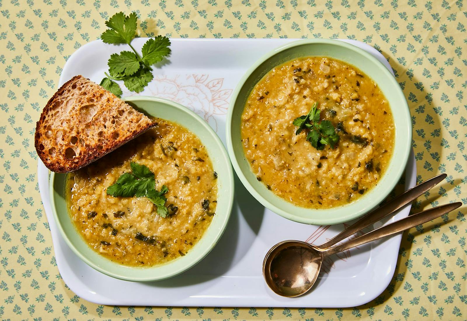 Two bowls of soup with cilantro, toasted bread, atop yellow and blue tablecloth.