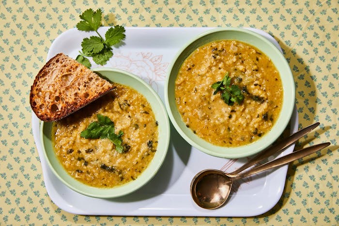 Two bowls of soup with cilantro, toasted bread, atop yellow and blue tablecloth.