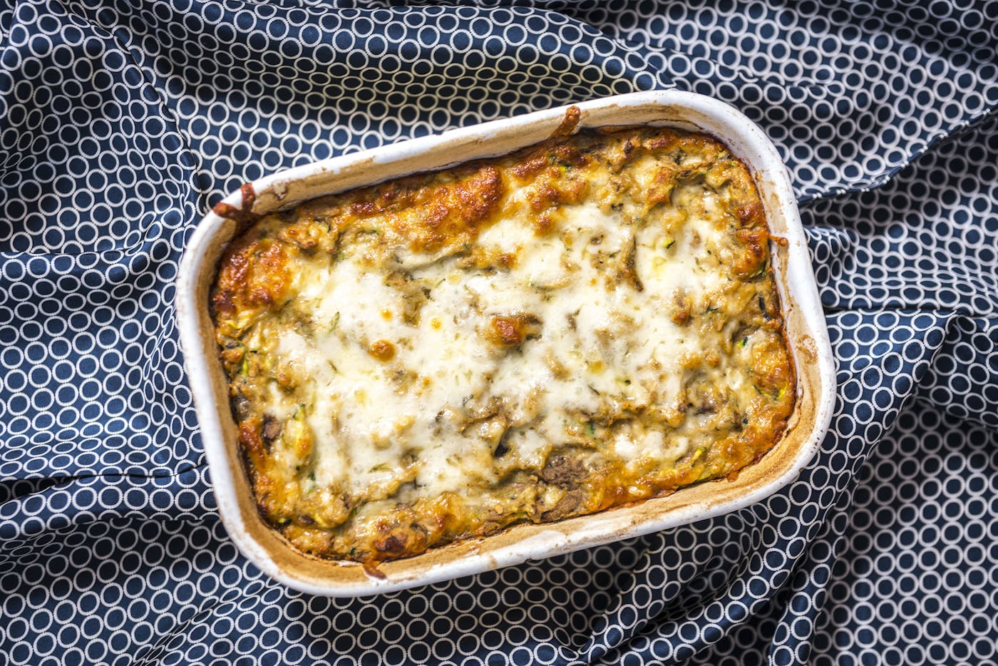 Roasted eggplant and kashkaval pie in white baking dish atop blue and white tablecloth.