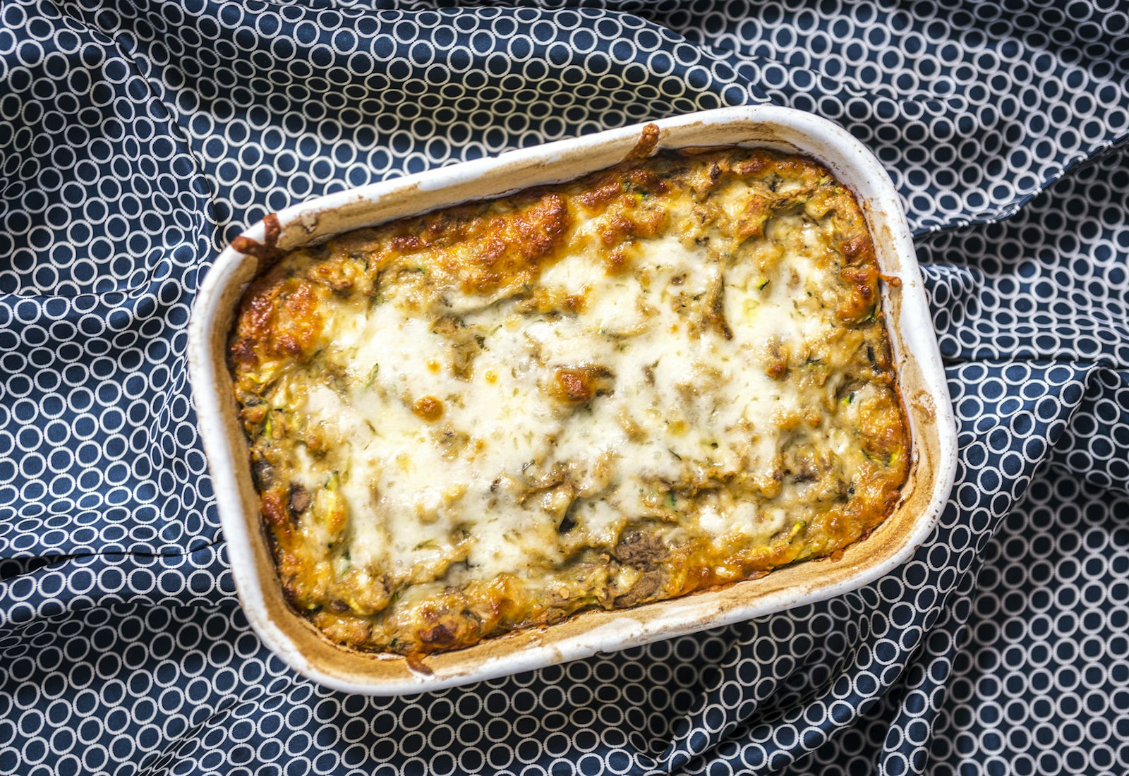Roasted eggplant and kashkaval pie in white baking dish atop blue and white tablecloth.