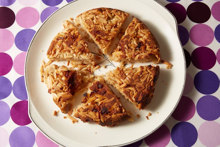 Apple and almond kugel sliced into portions on white plate atop purple-patterned tablecloth.