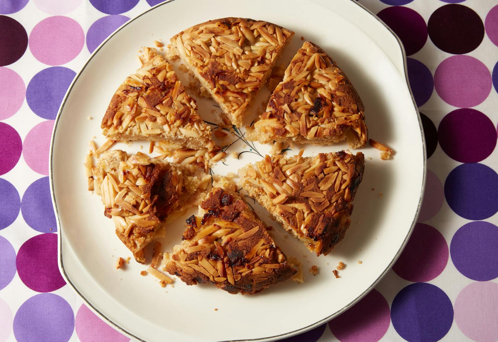 Apple and almond kugel sliced into portions on white plate atop purple-patterned tablecloth.