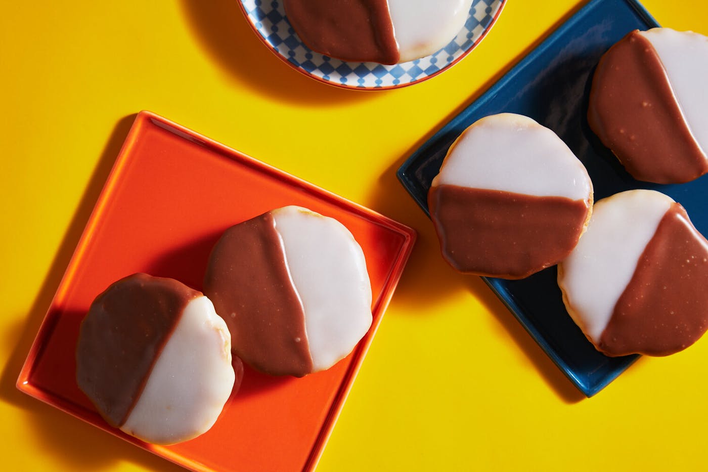 Black and white cookies on various colorful plates atop yellow surface.