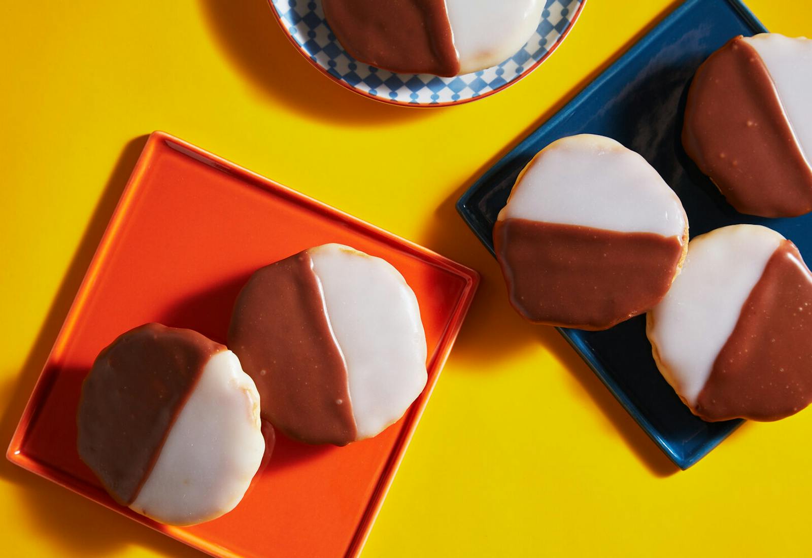 Black and white cookies on various colorful plates atop yellow surface.