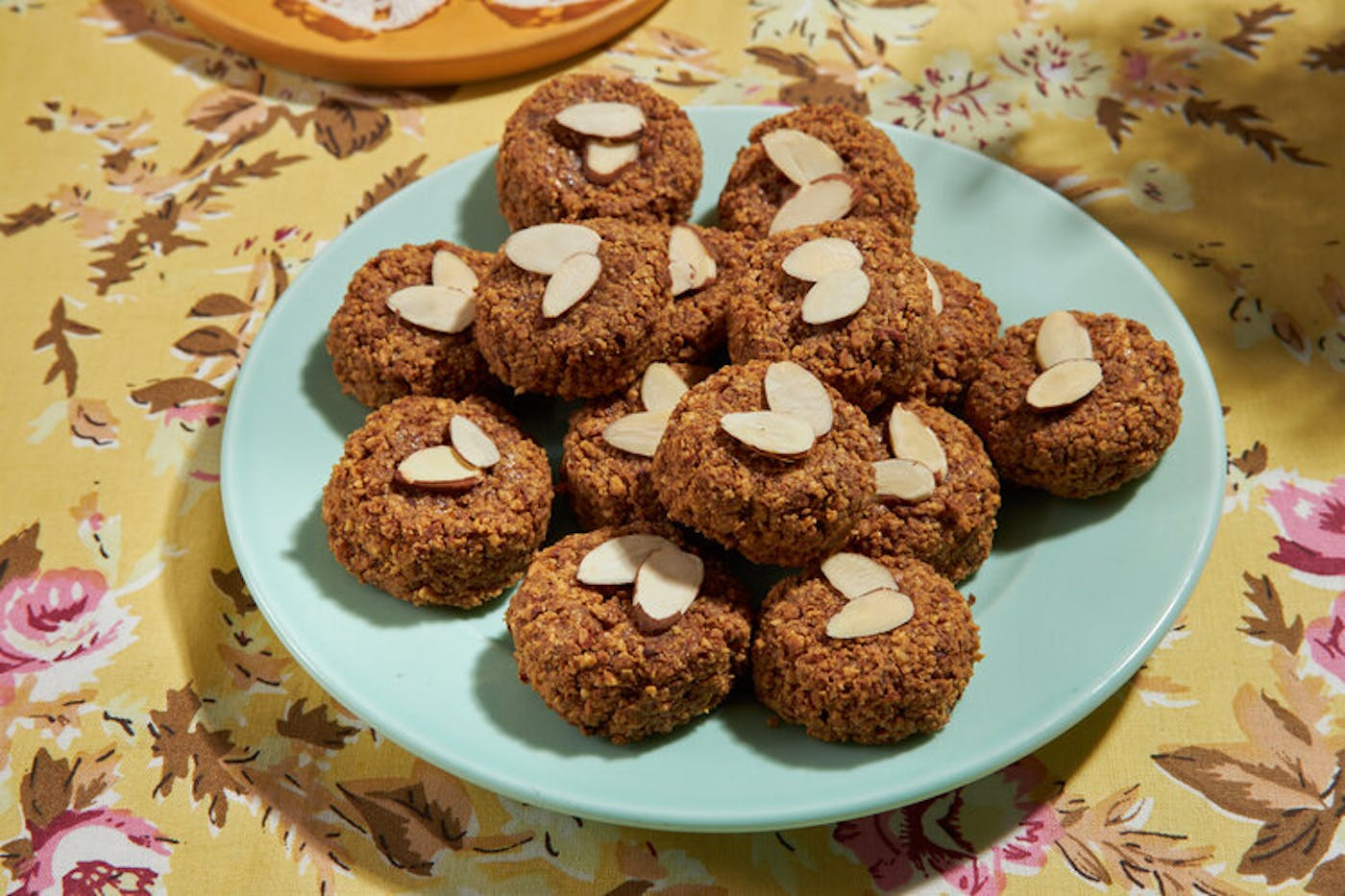 Macaroons with slivered almonds on blue plate atop yellow floral tablecloth.