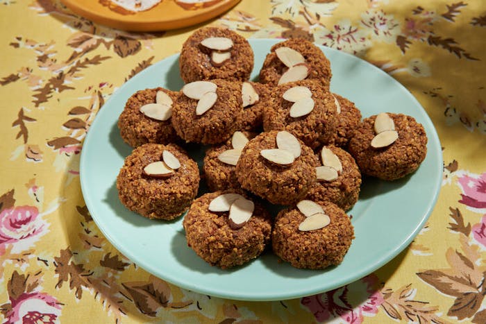 Macaroons with slivered almonds on blue plate atop yellow floral tablecloth.