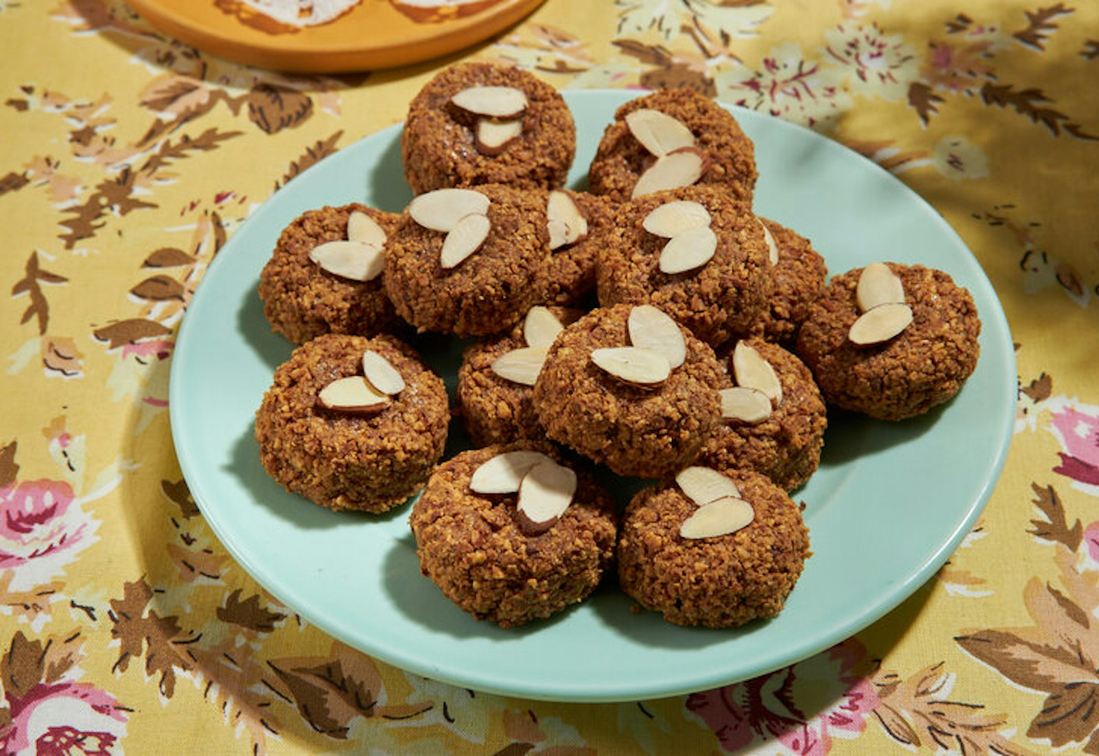 Macaroons with slivered almonds on blue plate atop yellow floral tablecloth.