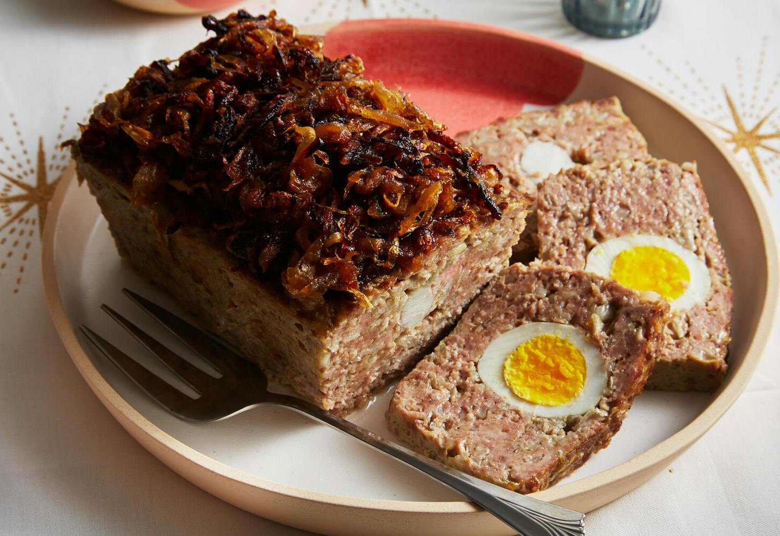 Meatloaf topped with caramelized onions on pink and tan plate, atop white tablecloth with star patterns.