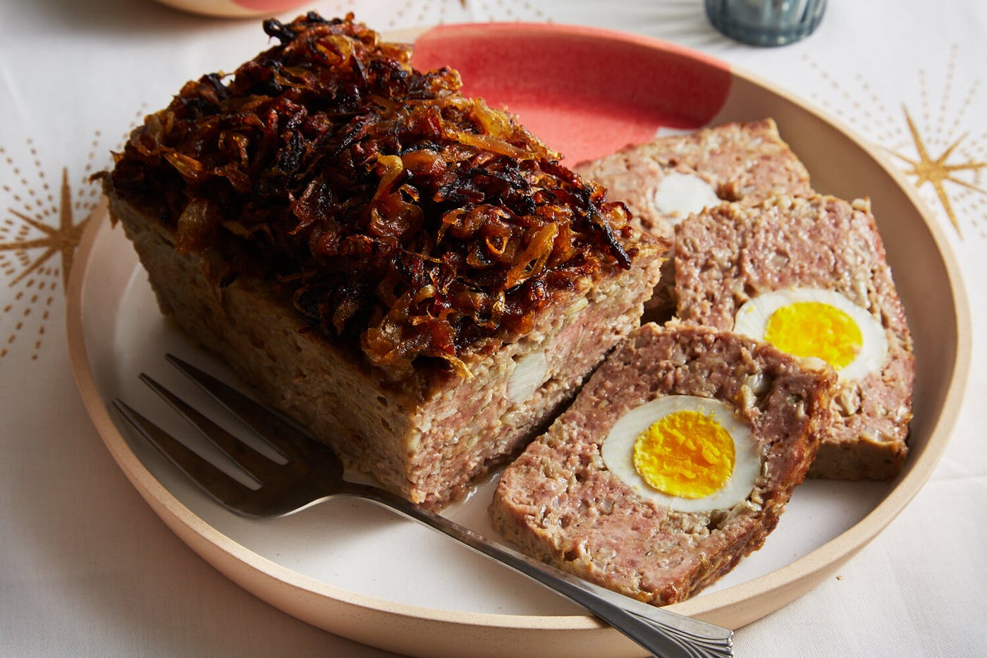 Meatloaf topped with caramelized onions on pink and tan plate, atop white tablecloth with star patterns.
