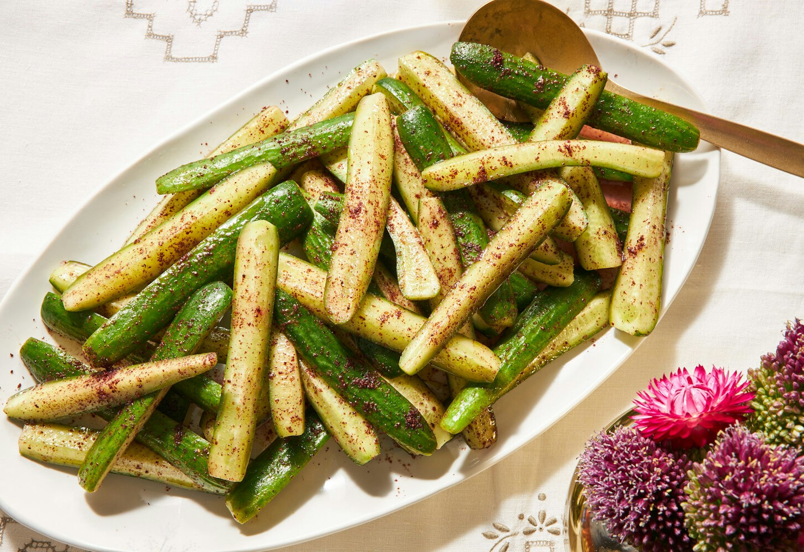 Cucumber salad on white dish with fresh flowers atop white patterned tablecloth.