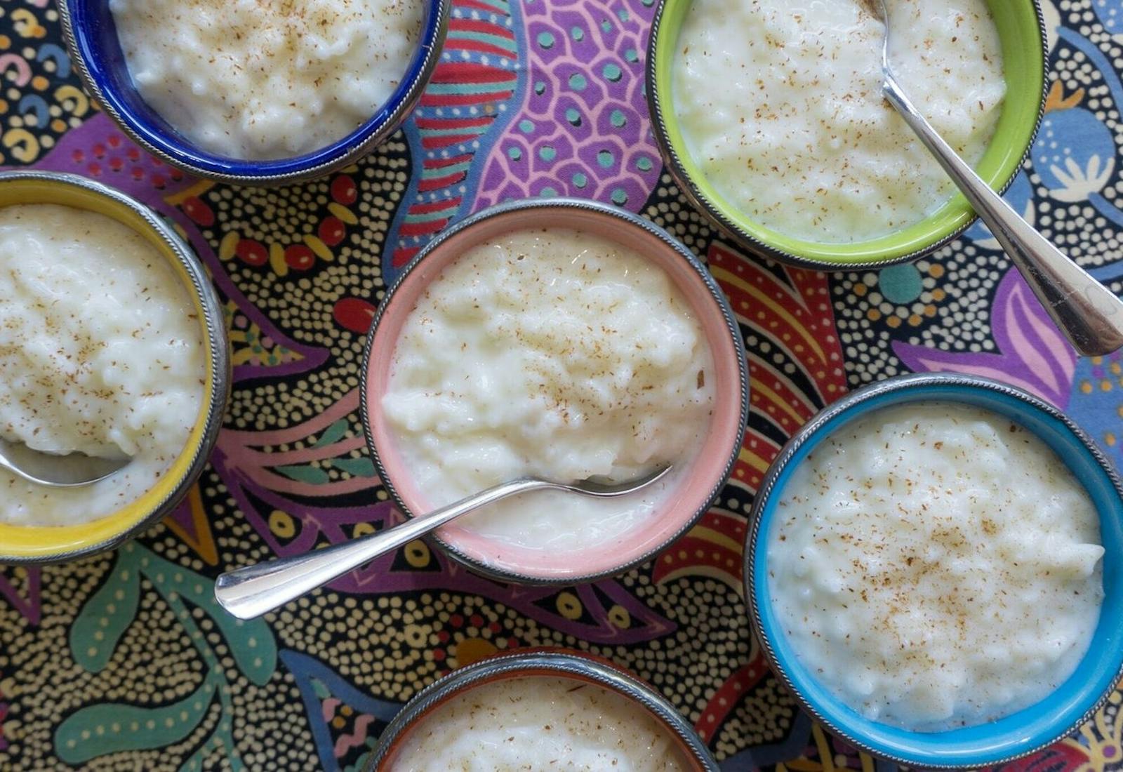 Colorful bowls filled with rice pudding garnished with cinnamon atop vibrant print tablecloth.