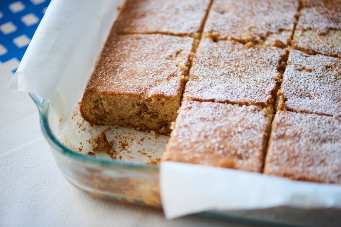 Sliced maple walnut cake in parchment lined baking dish, atop blue and white checkered tablecloth.