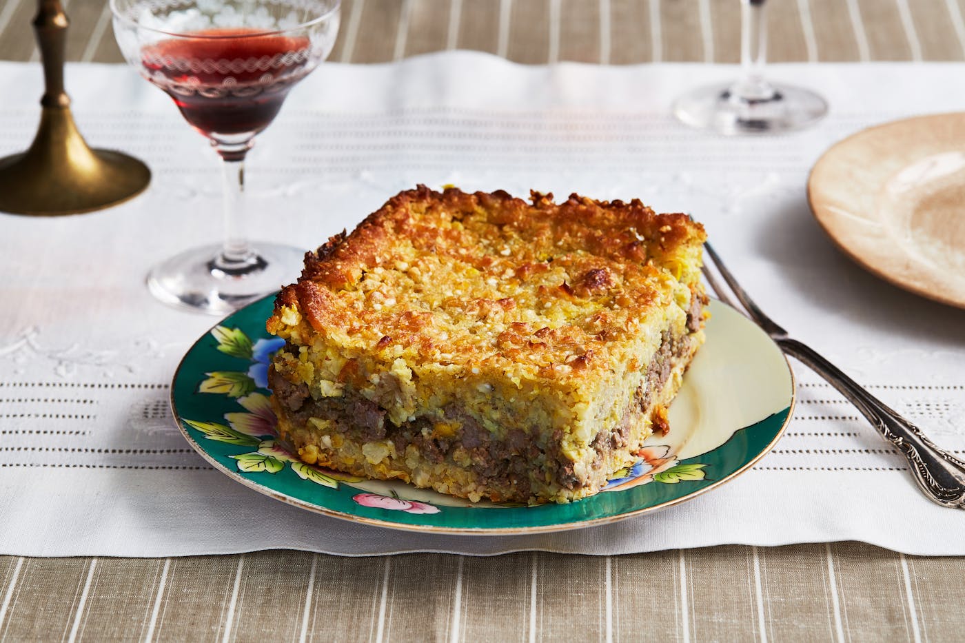 Pastel de Choclo on a plate next to a glass of red wine.