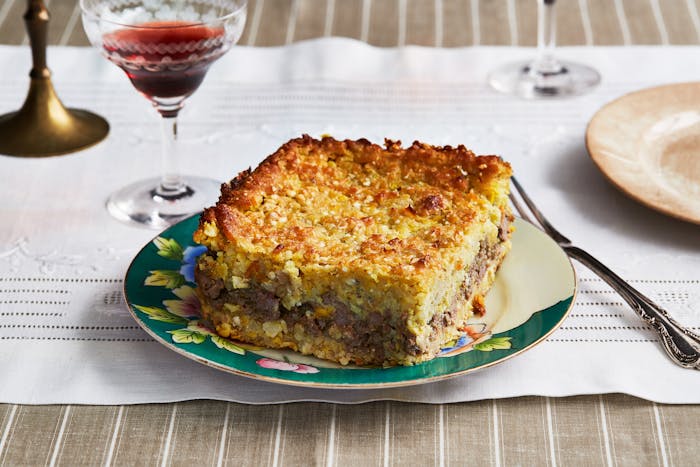 Pastel de Choclo on a plate next to a glass of red wine.