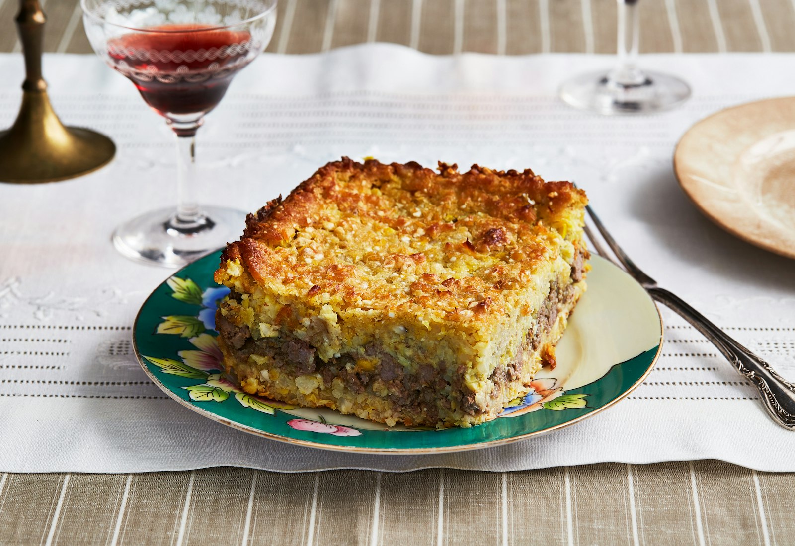 Pastel de Choclo on a plate next to a glass of red wine.