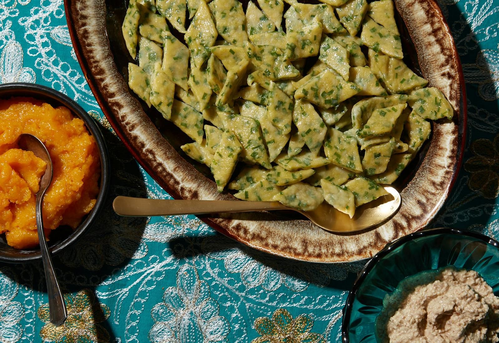 Ingar poli on serving dish alongside bowls of apricot and walnut sauces, atop blue tablecloth.