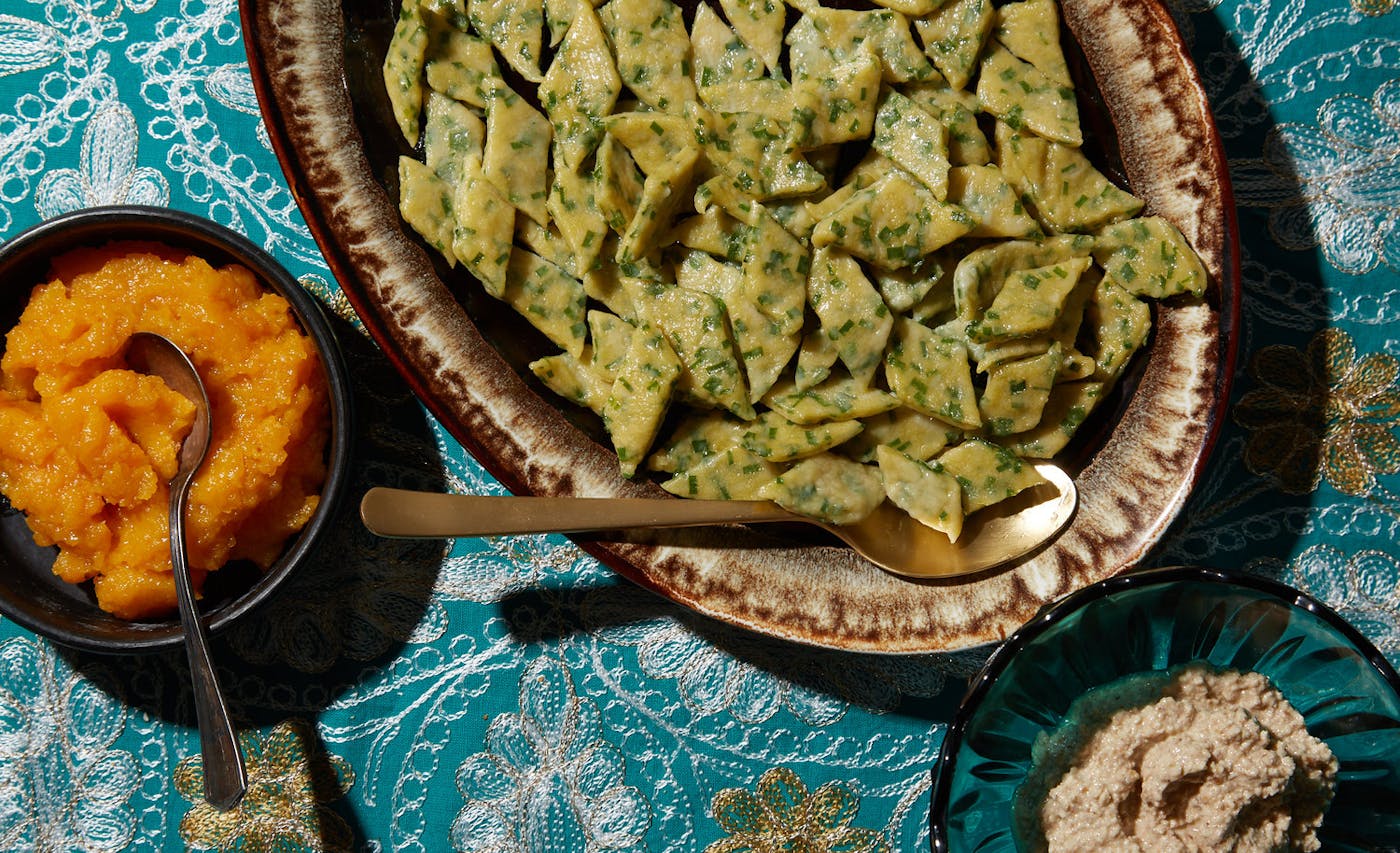 Ingar poli on serving dish alongside bowls of apricot and walnut sauces, atop blue tablecloth.
