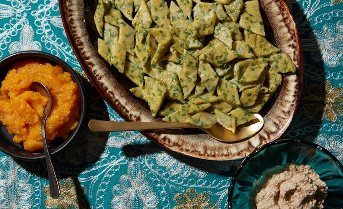 Ingar poli on serving dish alongside bowls of apricot and walnut sauces, atop blue tablecloth.