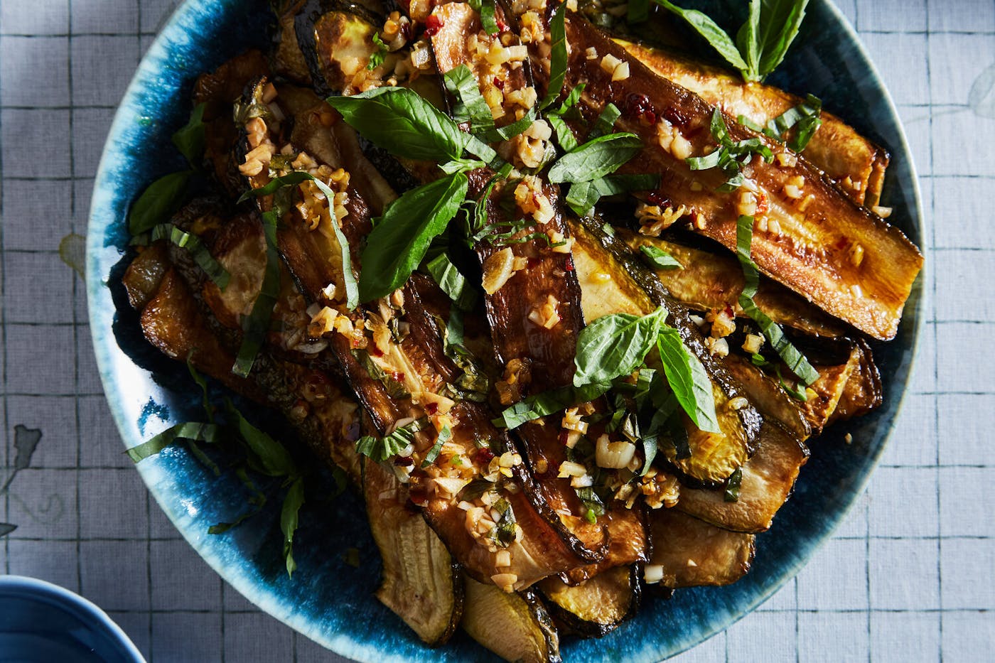 Concia garnished with basil leaves in blue bowl atop grid-patterned tablecloth.