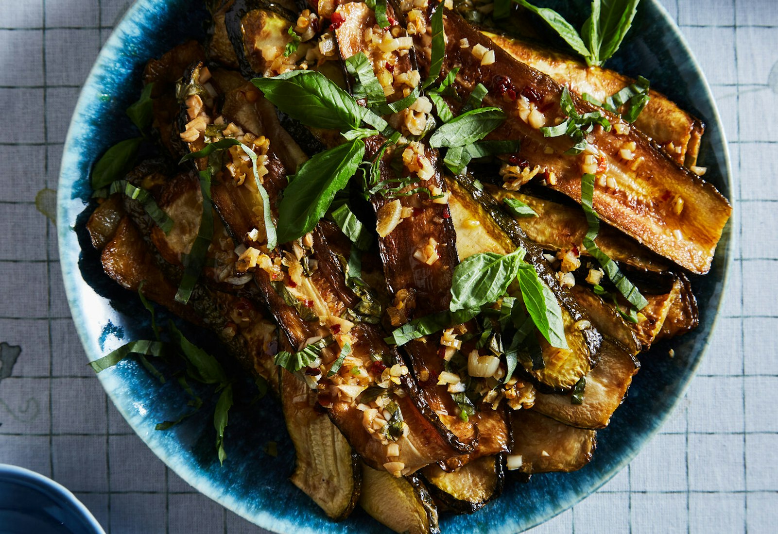 Concia garnished with basil leaves in blue bowl atop grid-patterned tablecloth.