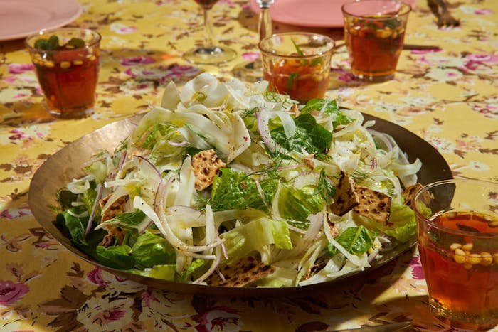 Lettuce and fennel salad garnished with pieces of matzo, mint tea atop yellow floral tablecloth.