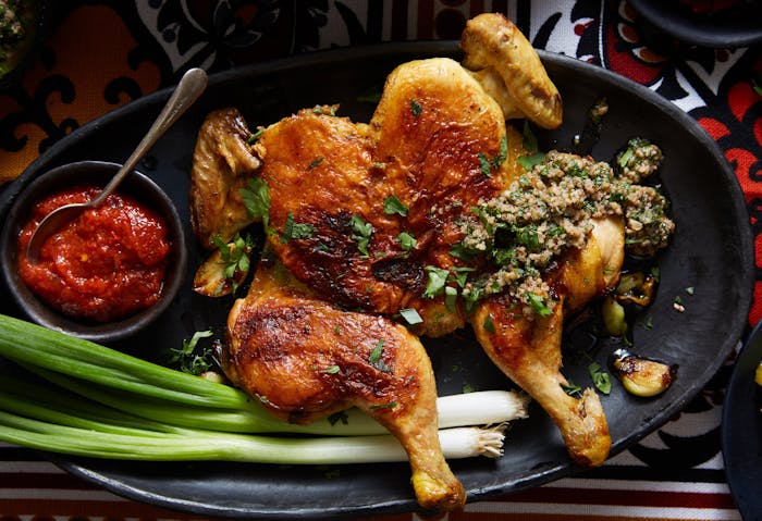 Pan fried cornish hen with radishes,  walnut garlic sauce and adjika sauce on black plate atop red and orange tablecloth.