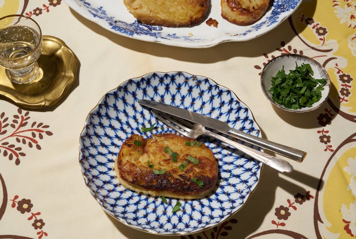 Stuffed chicken neck with chopped parsley alongside glass of vodka and dish of fresh parsley atop yellow floral tablecloth.