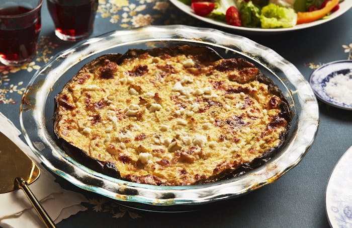 Patrician mi tiri in glass pie dish, red wine and green salad atop navy tablecloth.