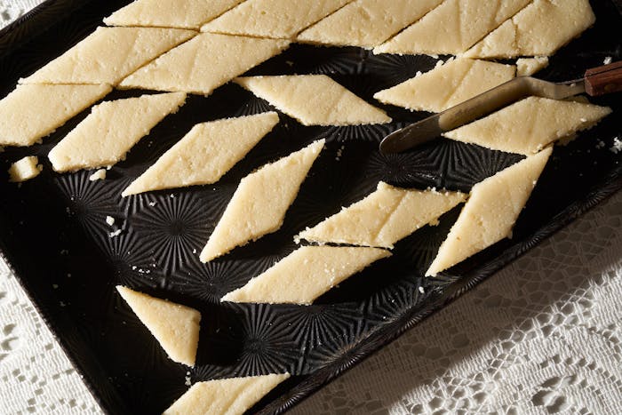 Marzipan sliced into diamonds on black pan atop white woven tablecloth.