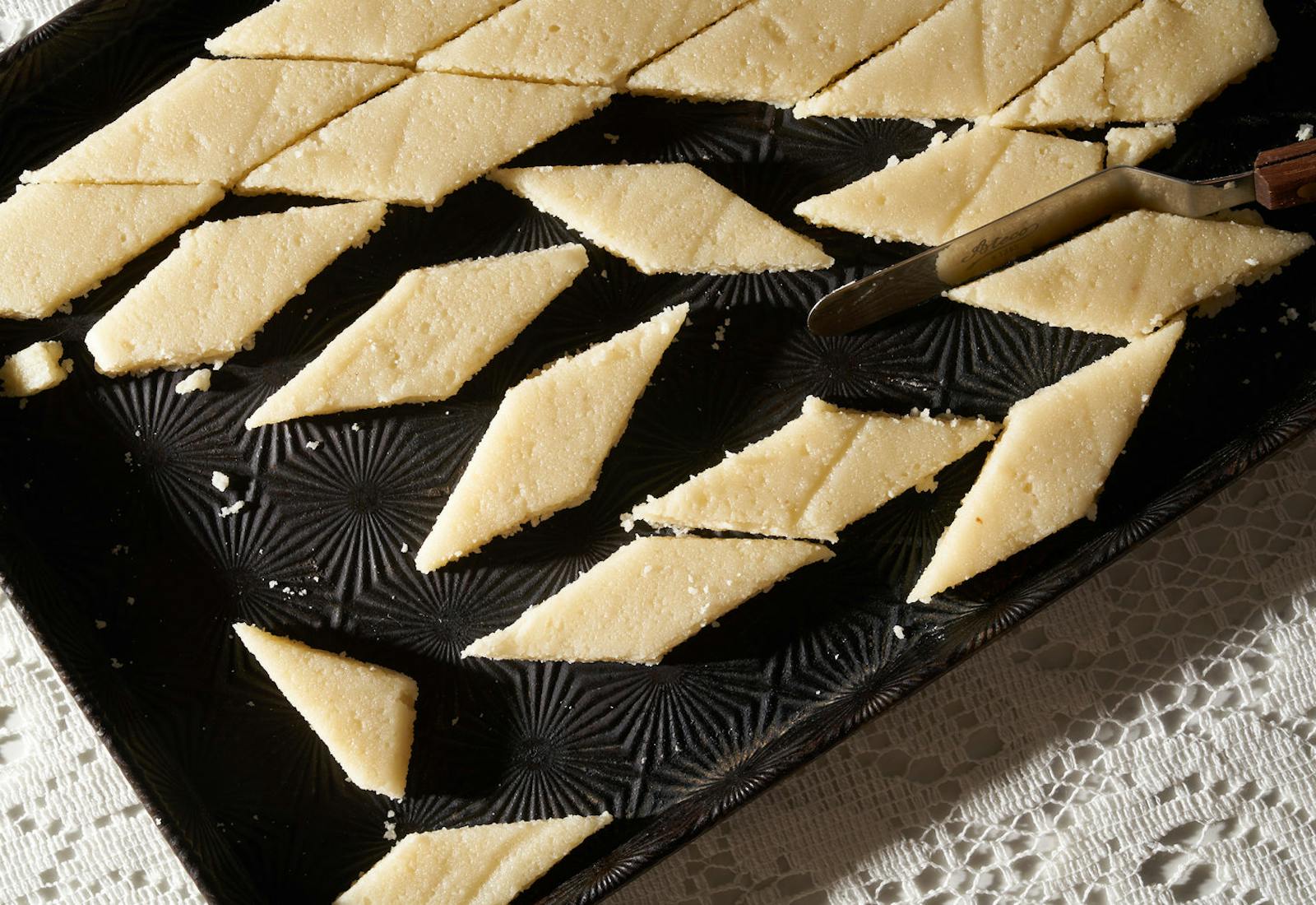 Marzipan sliced into diamonds on black pan atop white woven tablecloth.