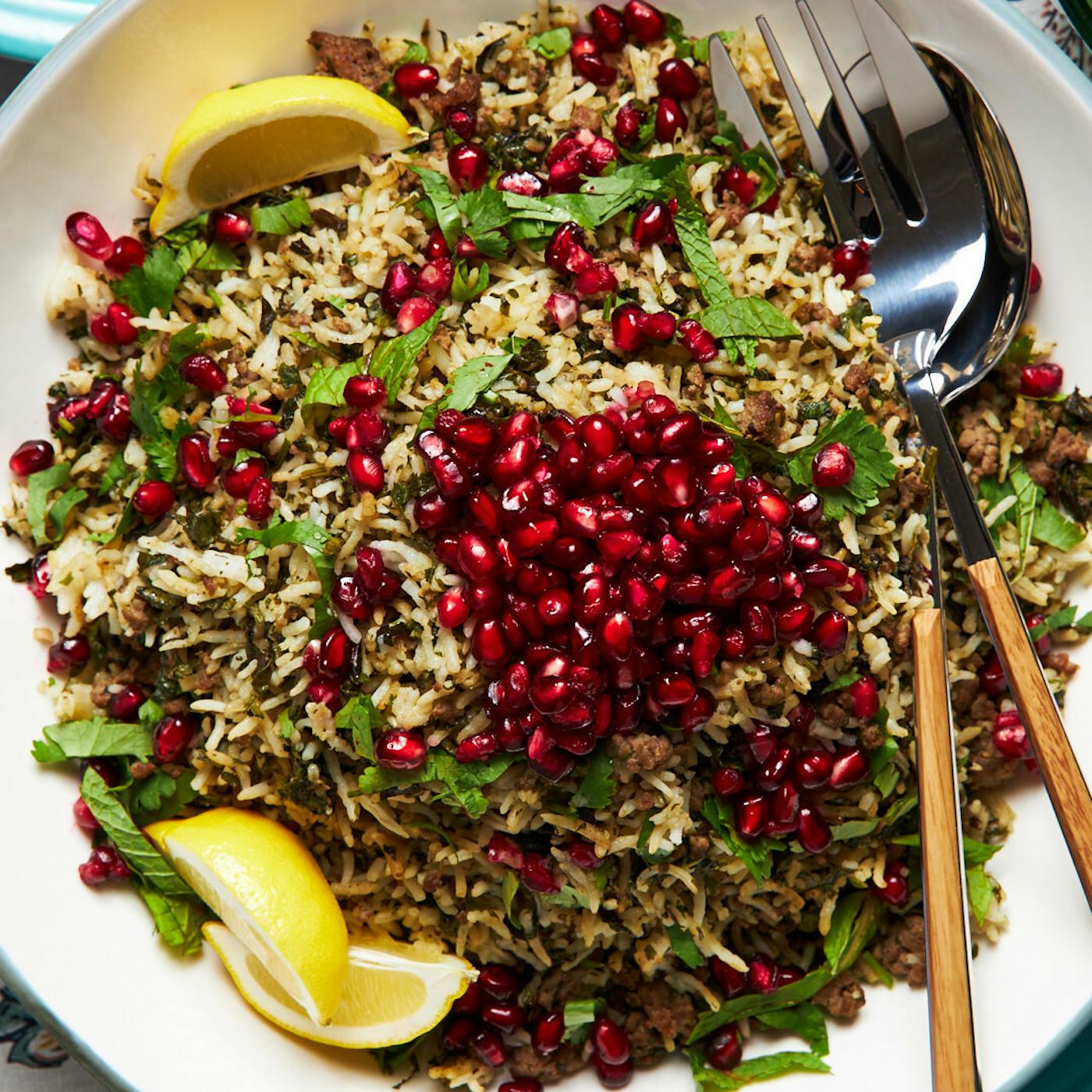 Oshi bakhsh garnished with pomegranate kernels and mint with lemon wedges.