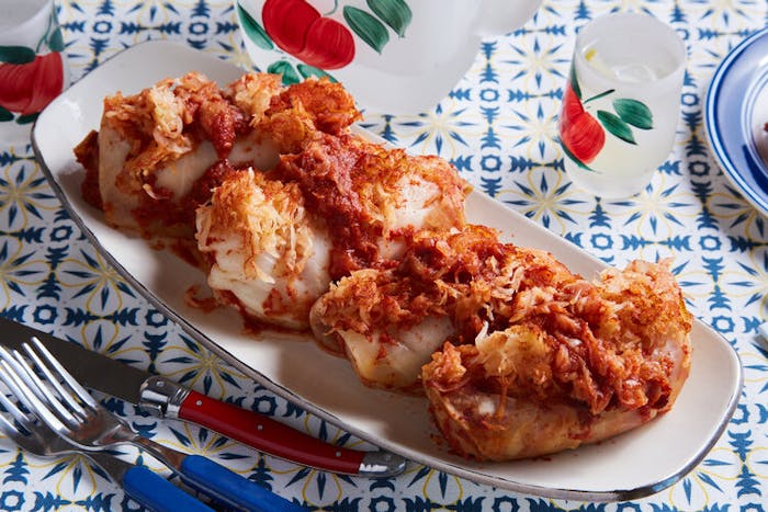 Stuffed cabbage topped with sauerkraut and tomato sauce alongside apple-printed cups. atop blue and yellow tablecloth.