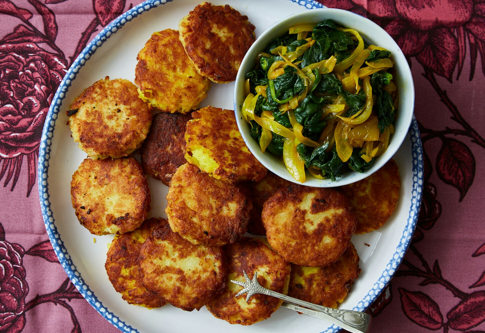 Shami with bowl of spinach and onion spread on large blue-patterned plate, atop pink floral tablecloth.