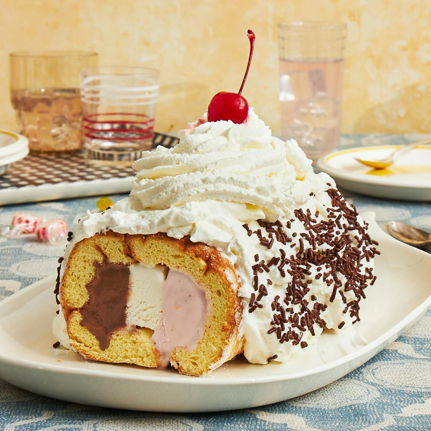 Neapolitan ice cream cake on white plate atop blue pattered tablecloth.
