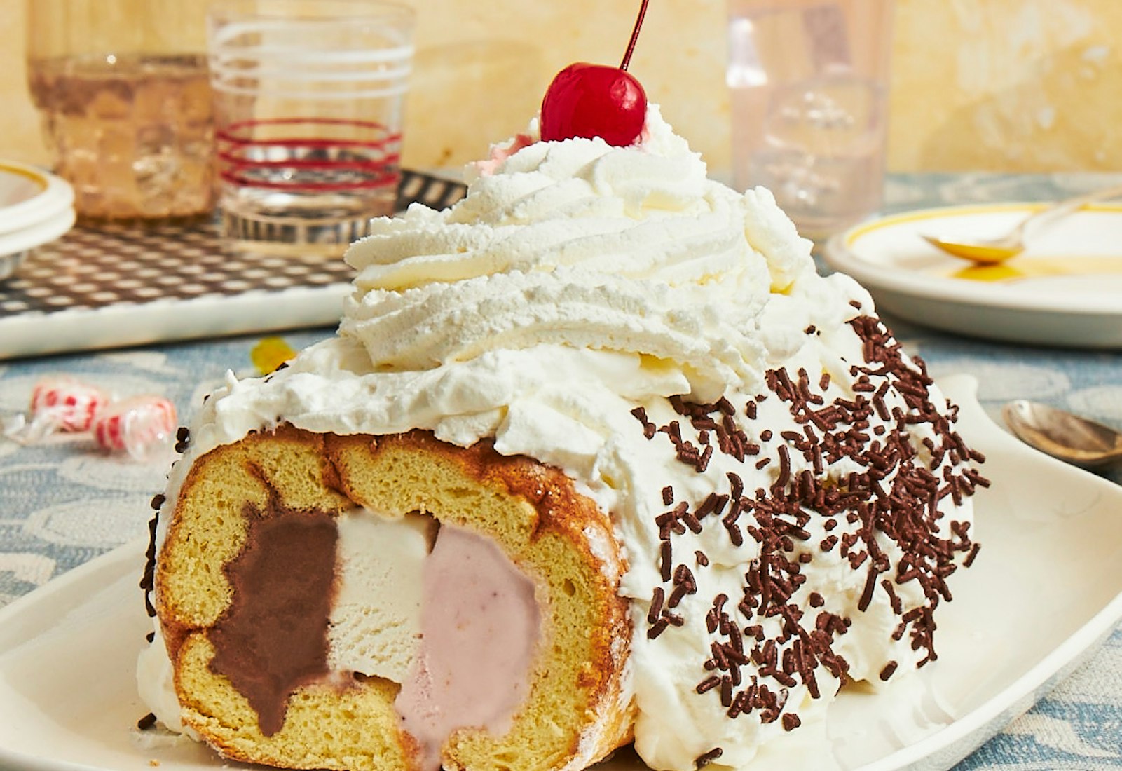 Neapolitan ice cream cake on white plate atop blue pattered tablecloth.
