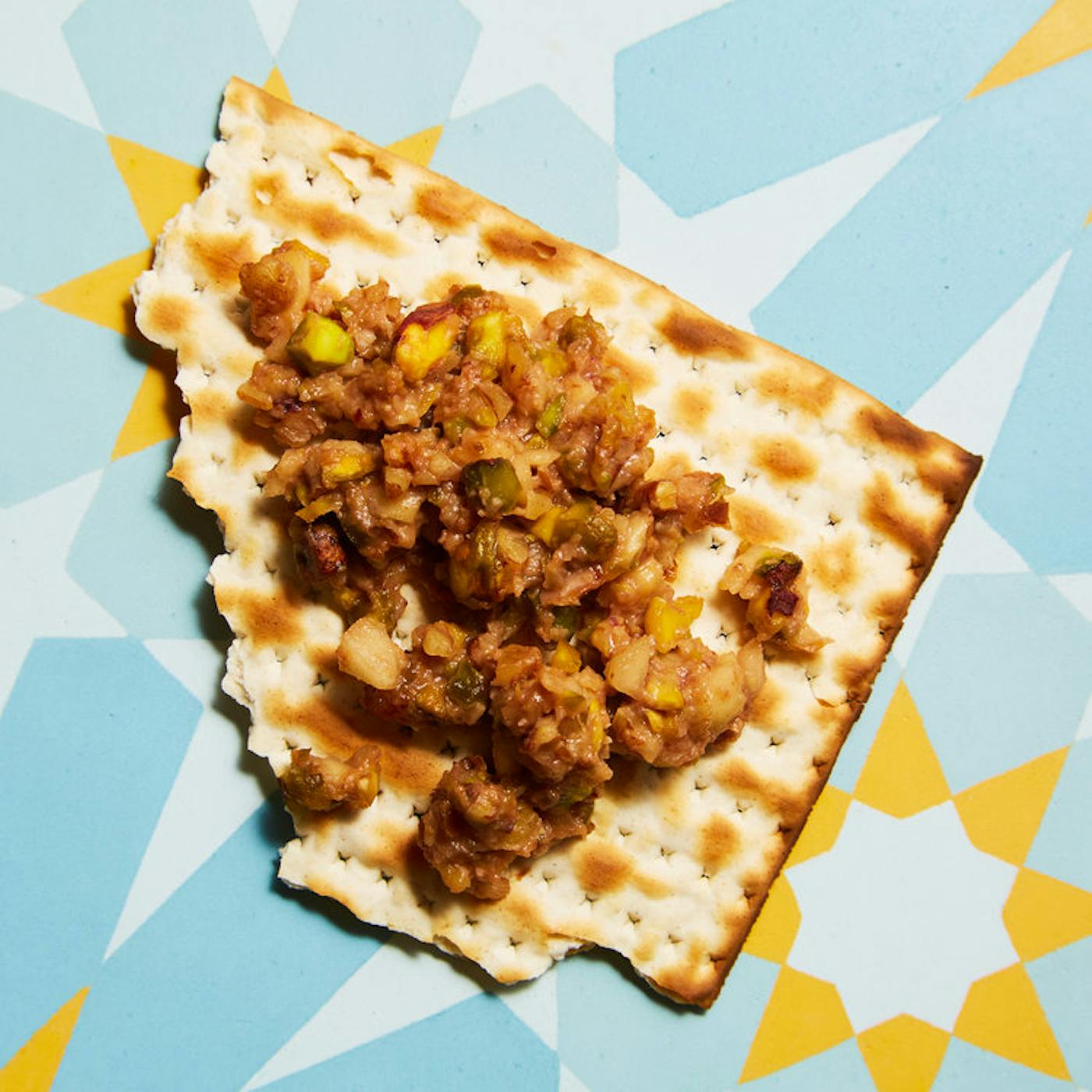 Scoop of Persian charoset on broken matzo bread atop bright blue and yellow surface.