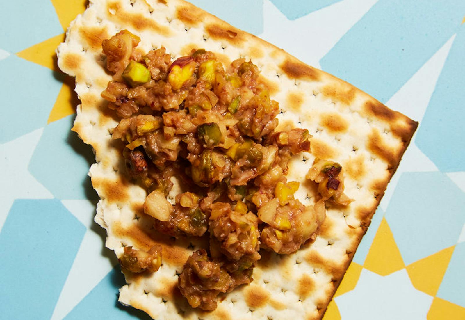 Scoop of Persian charoset on broken matzo bread atop bright blue and yellow surface.