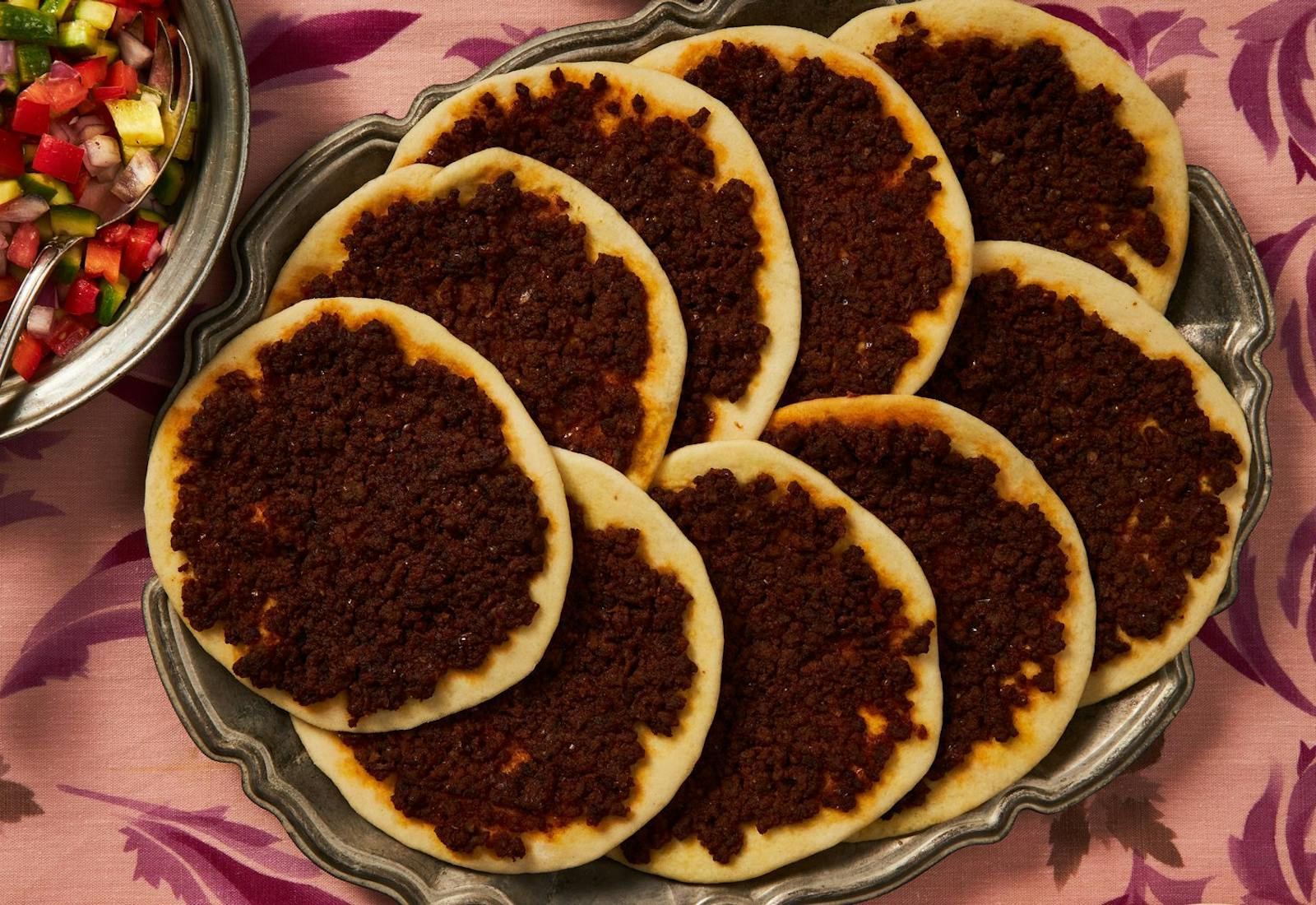 Laham b'Ajeen on a platter, side of chopped salad atop pink floral tablecloth.