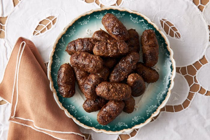 Merguez kebabs on blue plats atop white tablecloth.