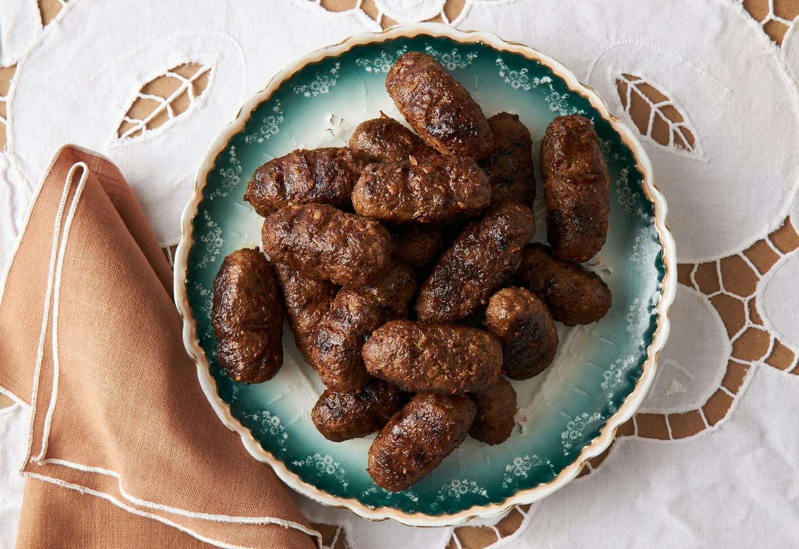 Merguez kebabs on blue plats atop white tablecloth.