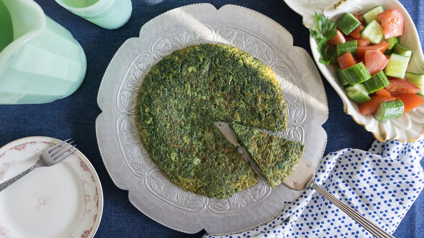 Kuku sabzi on flower-shaped plate alongside cucumber and tomato salad.