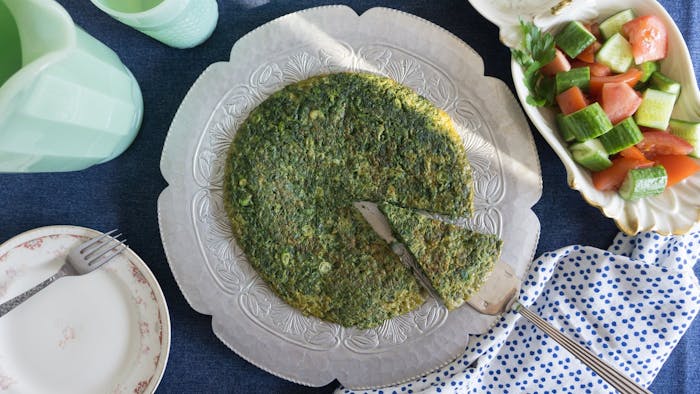 Kuku sabzi on flower-shaped plate alongside cucumber and tomato salad.