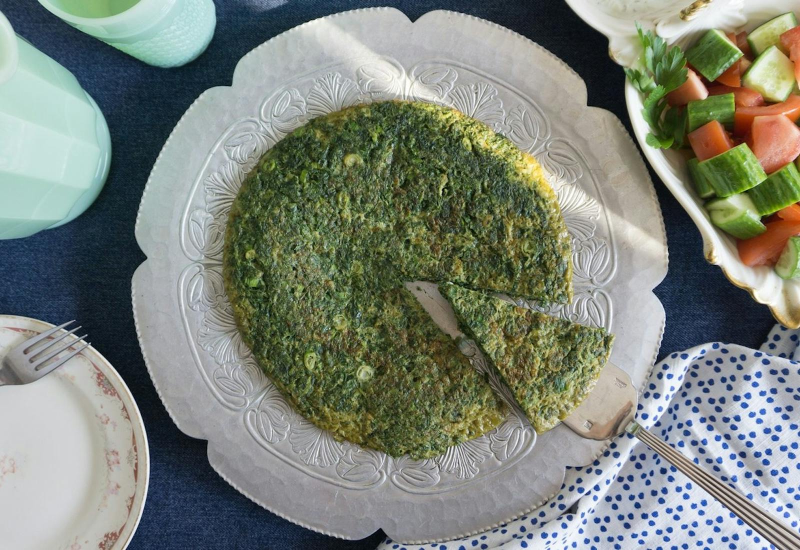 Kuku sabzi on flower-shaped plate alongside cucumber and tomato salad.