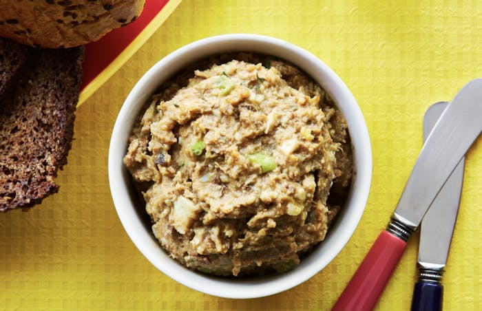 Chopped liver with slices of seeded bread atop yellow tablecloth.
